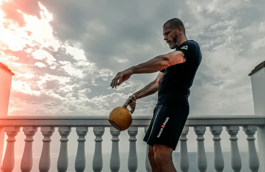 Man performing a Kettlebell Swing with a yellow kettlebell outdoors, demonstrating the hinge movement.