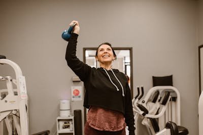 Woman performing a standing Overhead Press with a blue kettlebell for shoulder and core strength.