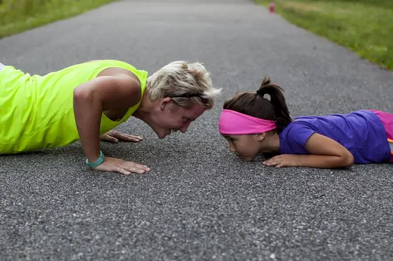 Young girl attempting push-ups, playfully challenged by an older woman.